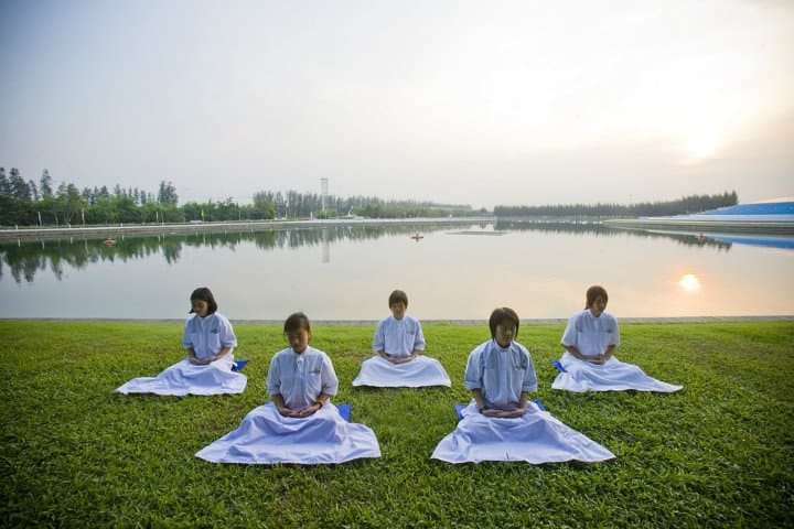 children meditating on the grass at a lake