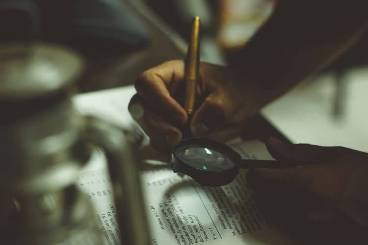 person writing with a magnyfing glass