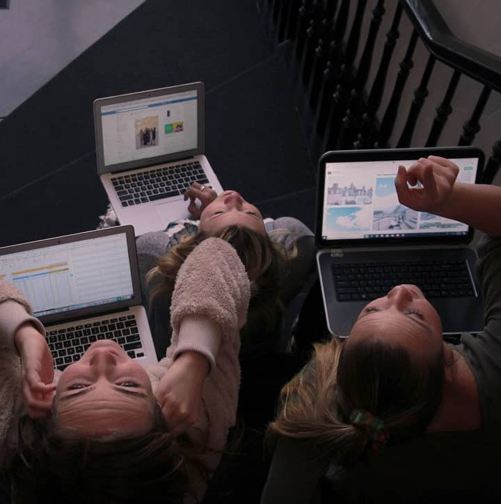 three girls with laptops on a staircase