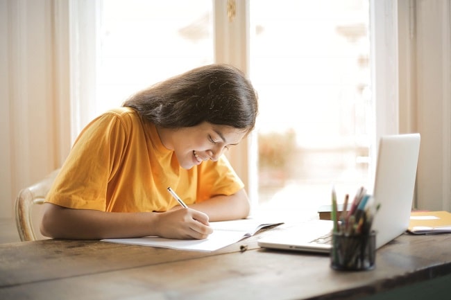 woman taking notes at a table with a laptop