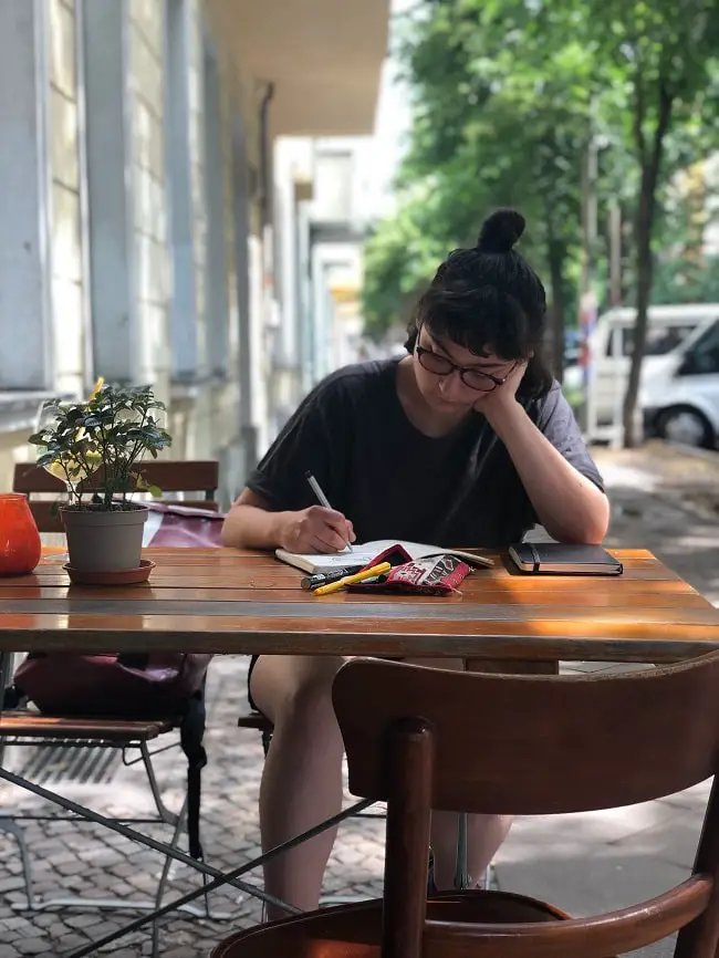 Girl writing in a notebook in an outside cafe