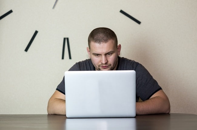 man typing with a huge clock in the background