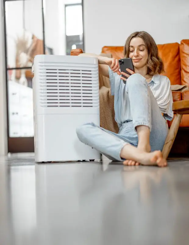 woman sitting next to a dehumidifier and using her mobile phone