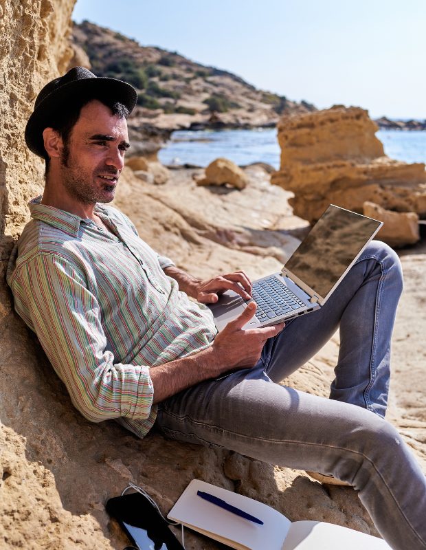 a writer sitting on a beach with a laptop