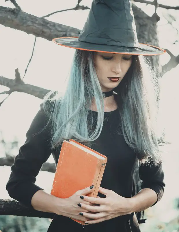 young adult female dressed as a witch and holding a book
