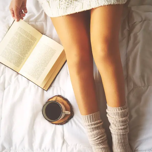 a cozied up girl reading a book in bed