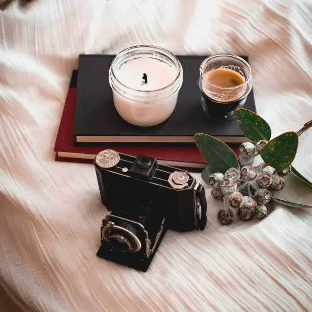 two books, a candle, a coffee, and an old camera on a bed